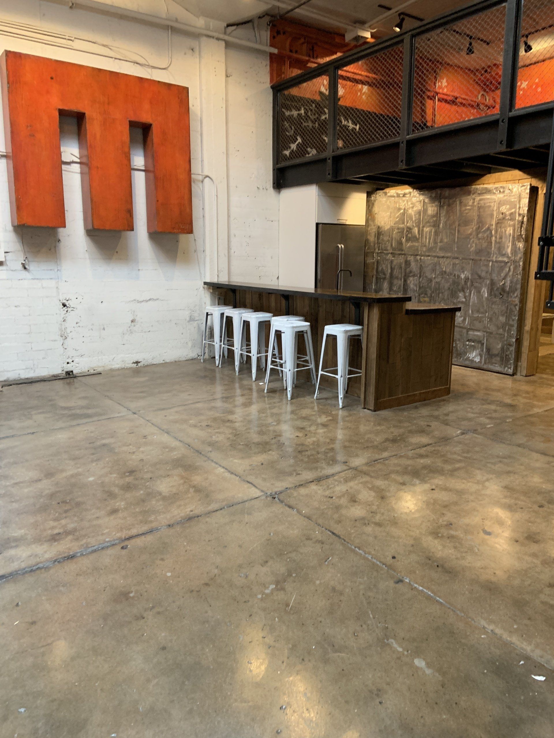 A row of white stools are lined up in a room with a large m on the wall.