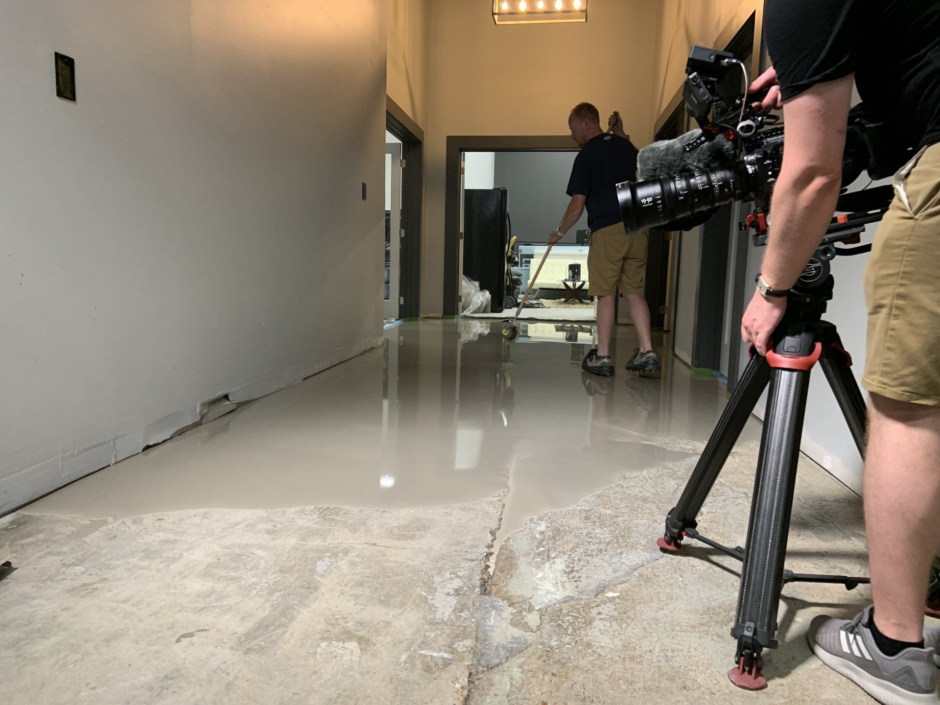 A man is standing in a hallway with a camera on a tripod.