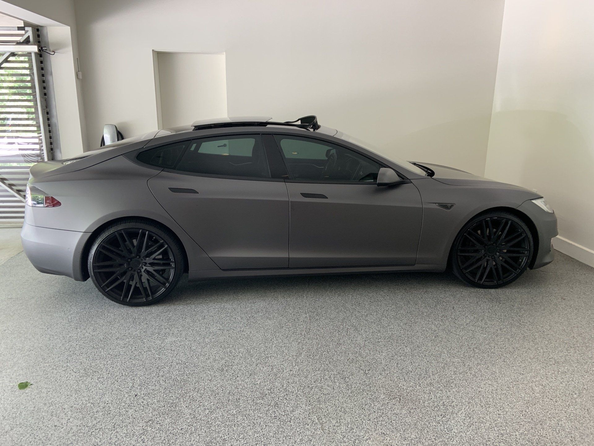 A gray tesla model s is parked in a garage.
