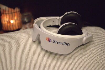 BrainTap headphones on a textured surface, with a lit candle blurred in the background