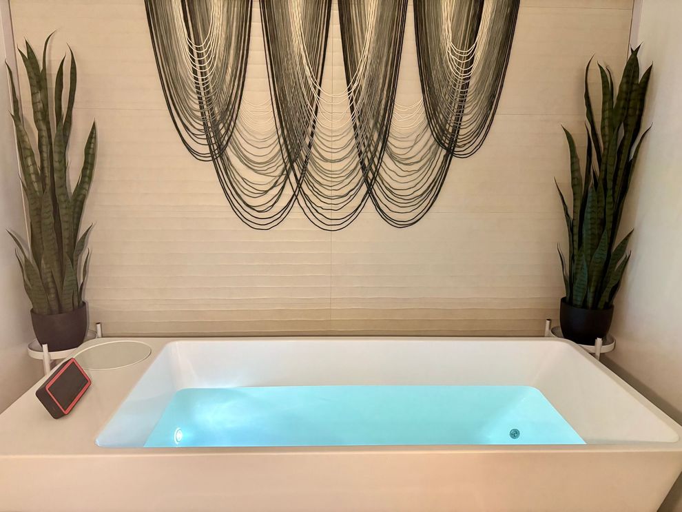 Modern spa tub with glowing blue water, flanked by tall plants and wall art
