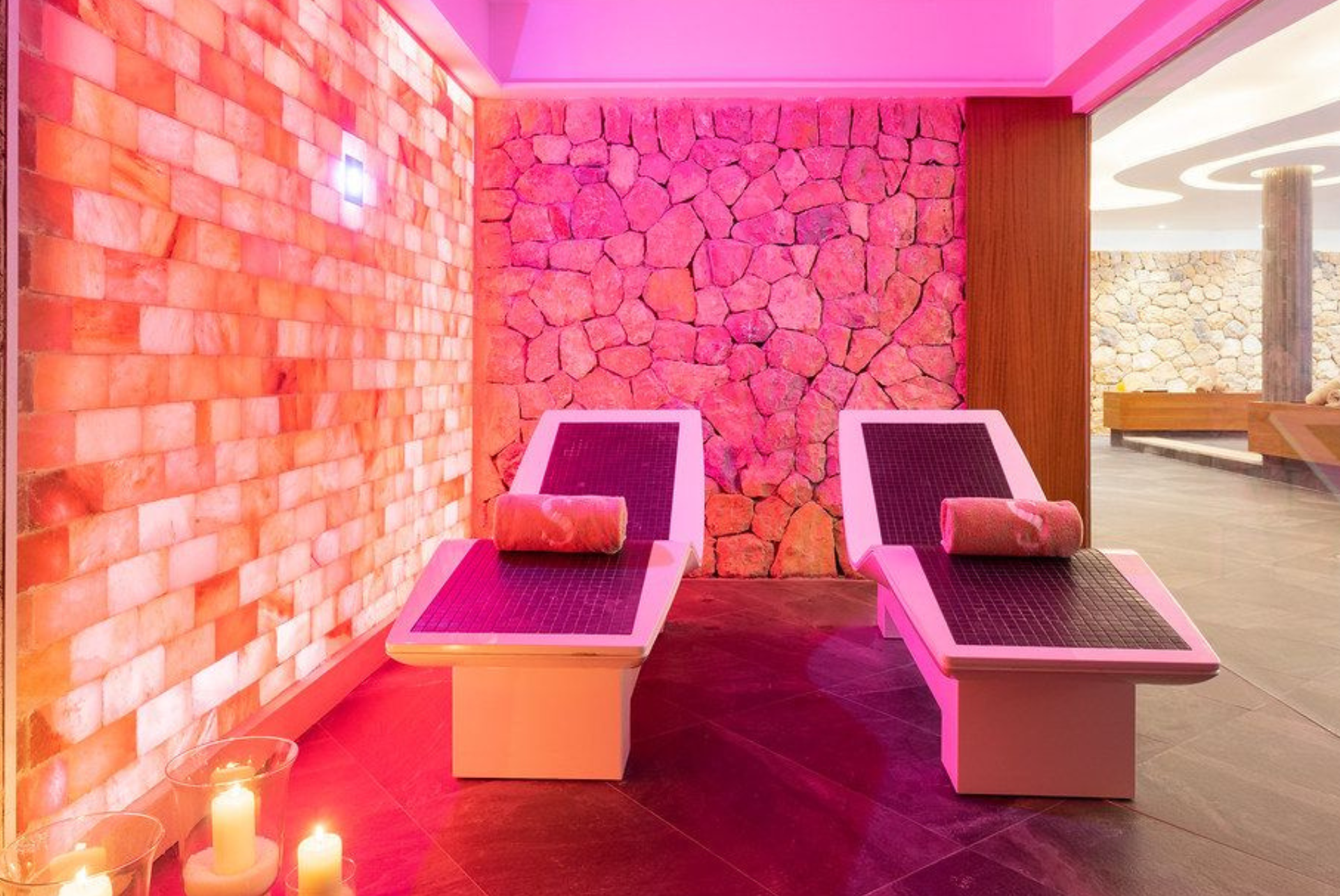 Pink-lit spa room with two white lounge chairs facing a stone accent wall
