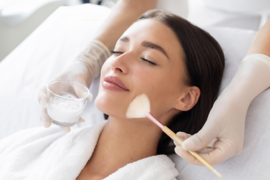 Woman receiving a facial treatment with a brush and cream in a spa setting