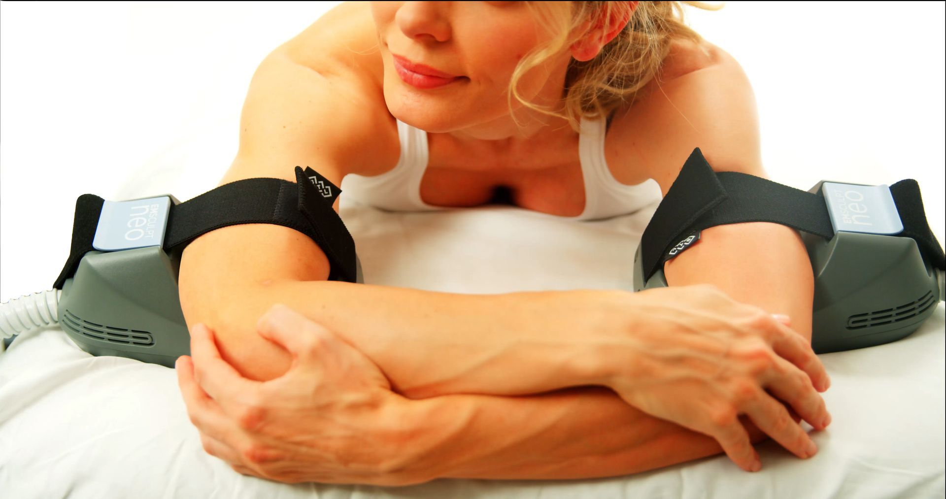 Woman leaning on a white bed between black massage devices, resting with a relaxed expression