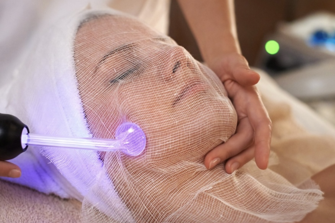 Woman receiving a facial treatment with a glowing purple device on her cheek