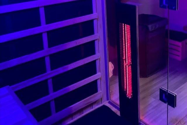 Purple-lit sauna or infrared heater beside glass panels and wooden slats