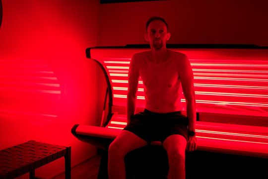 Person sitting on a bench in a red-lit room with horizontal light strips on the wall.