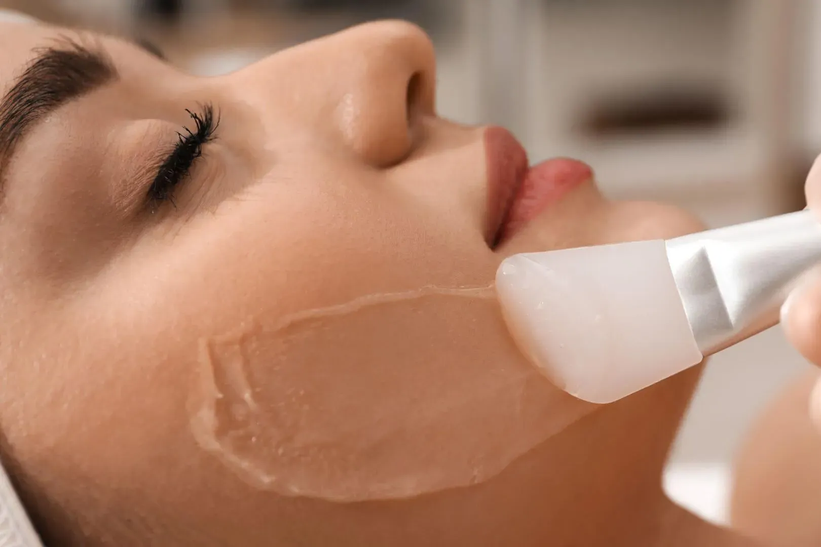 Close-up of a facial mask being applied to a person’s cheek with a brush