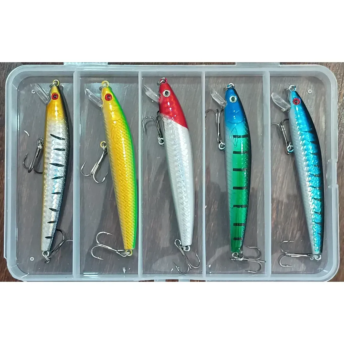 Cinco señuelos de pesca de colores en una caja transparente con compartimentos individuales