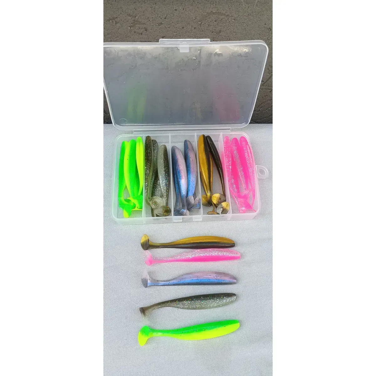 Caja de pesca transparente con señuelos blandos de colores sobre una superficie de madera