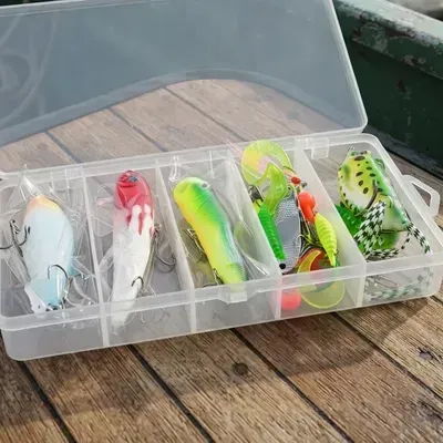 Caja de plástico para aparejos de pesca con cinco señuelos de colores sobre una mesa de madera al aire libre