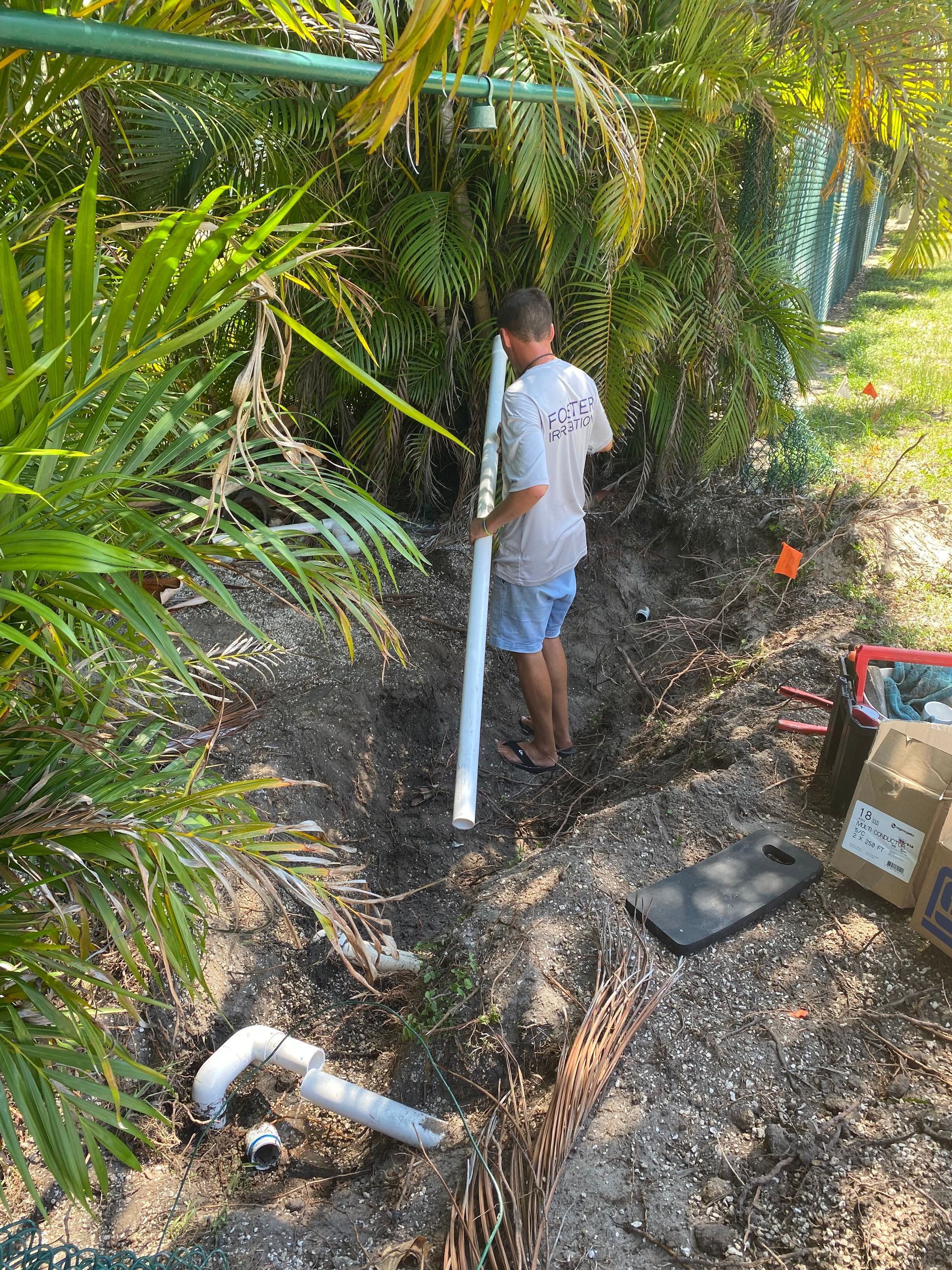 A man is standing in the dirt holding a pipe.