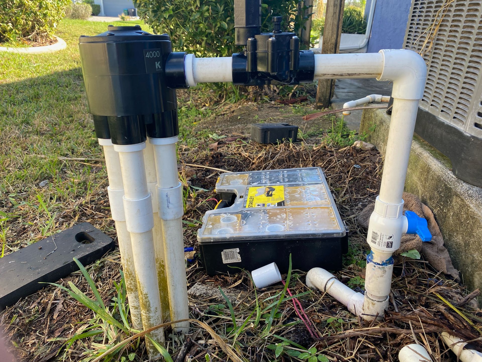 A water pump is sitting in the grass next to a house.