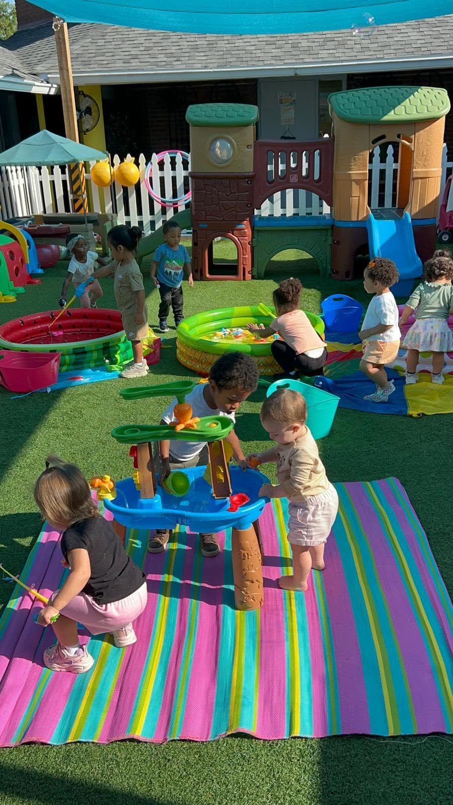 Children playing at outdoor water tables on colorful rugs in a playground area