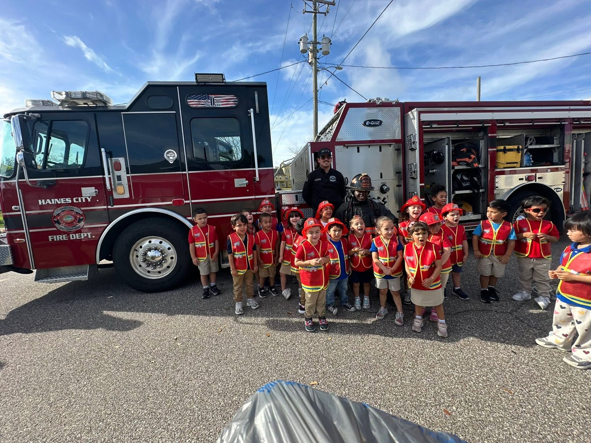 Children in red life jackets posing with firefighters and fire trucks outdoors