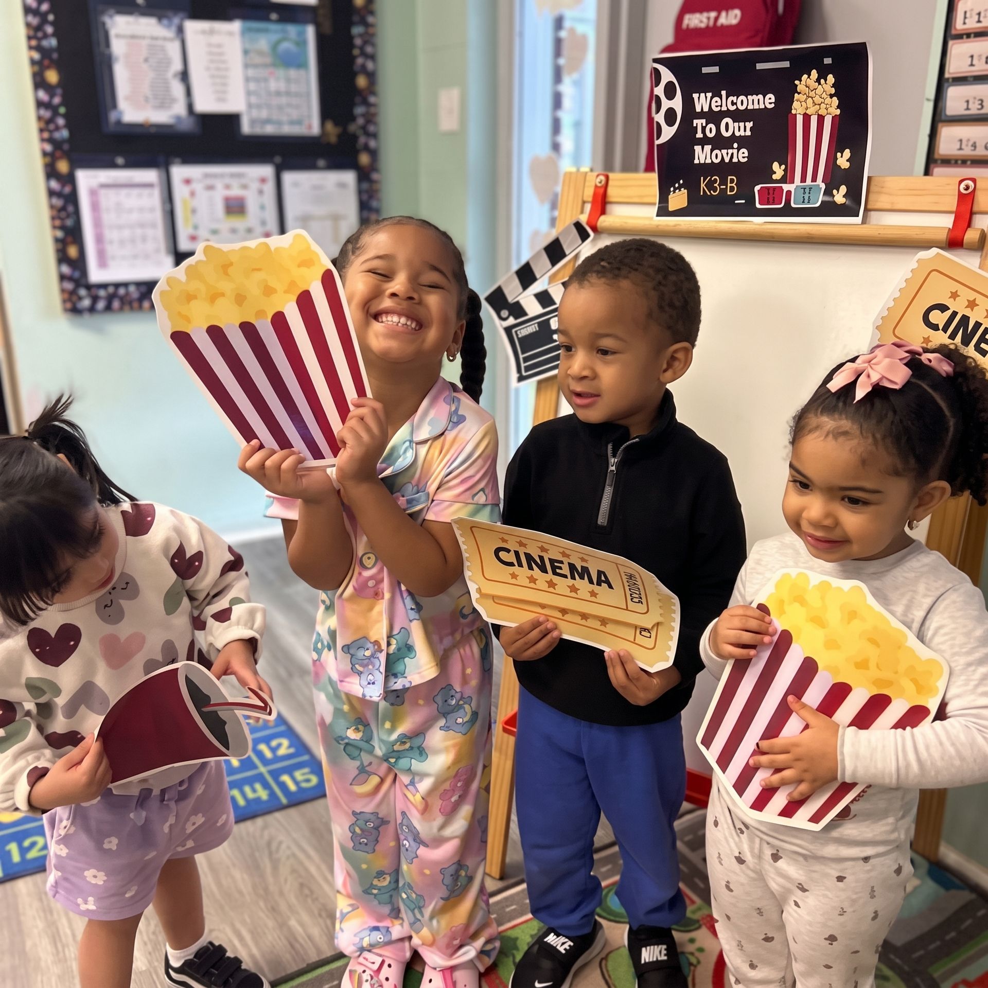 Children in a movie-themed play area holding popcorn and cinema signs, smiling and posing.