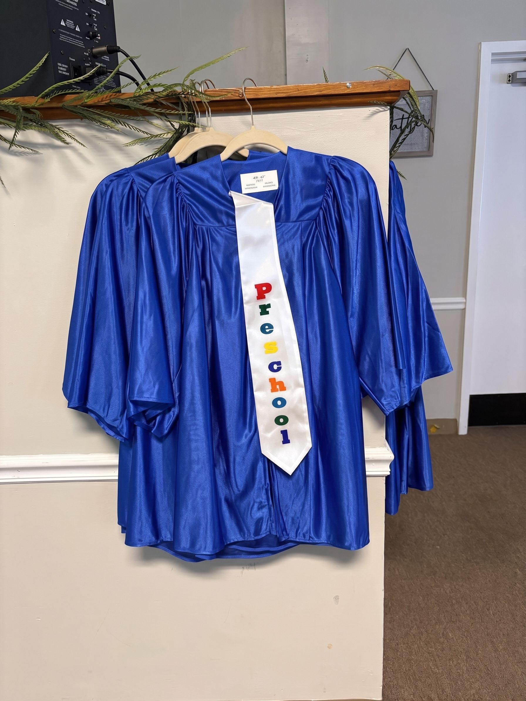 Blue graduation gown with a white tie hanging on a wall in an indoor hallway.