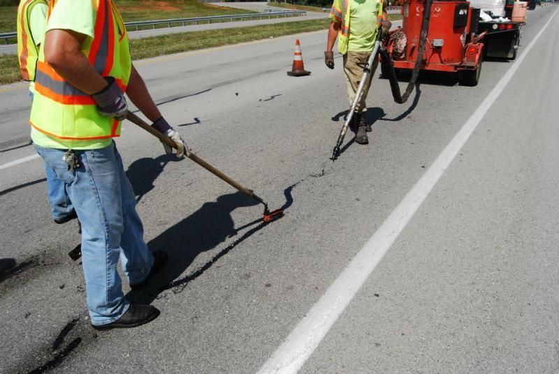A man is spreading asphalt on a road next to a traffic cone