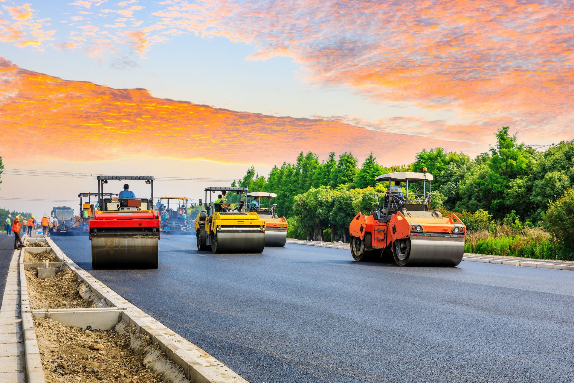 A row of asphalt rollers are working on a road under construction