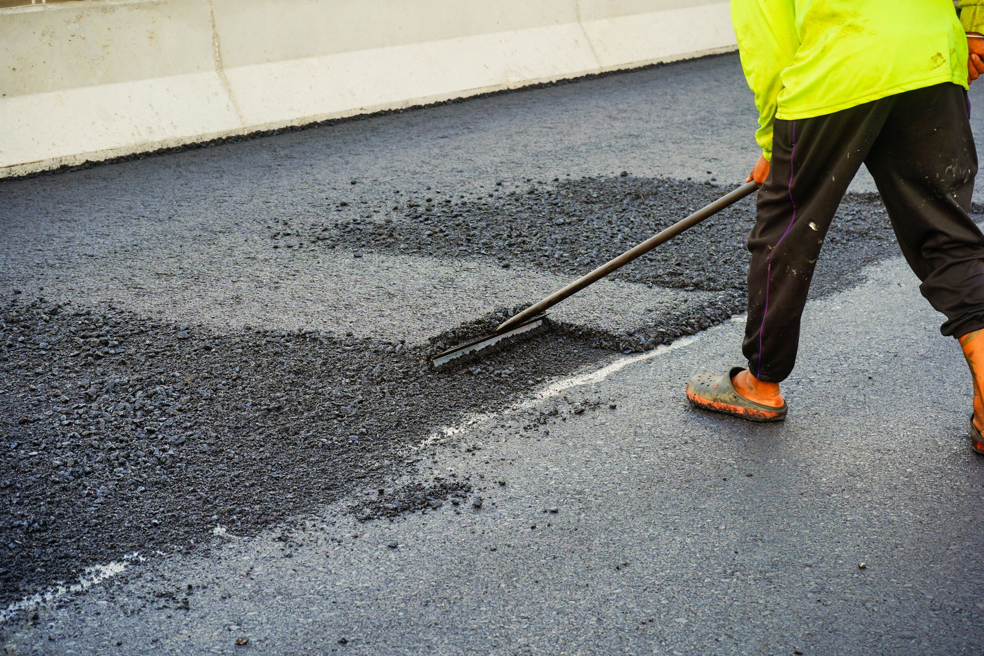 A man is spreading asphalt on a road with a rake