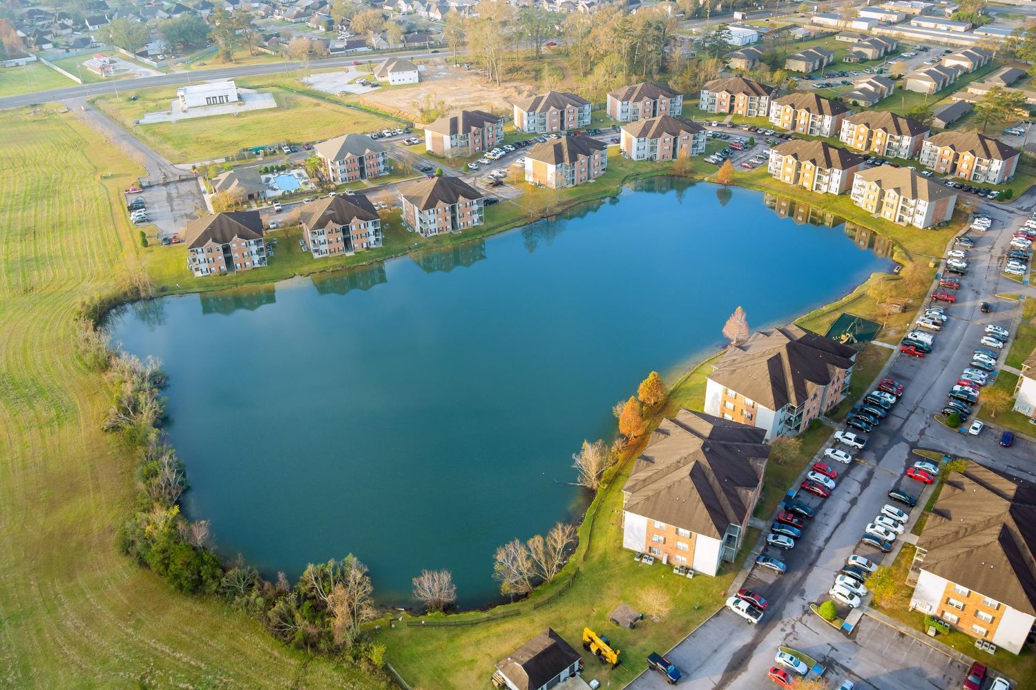 Aerial view of a pond surrounded by homes, roads, and green fields in a suburban neighborhood.