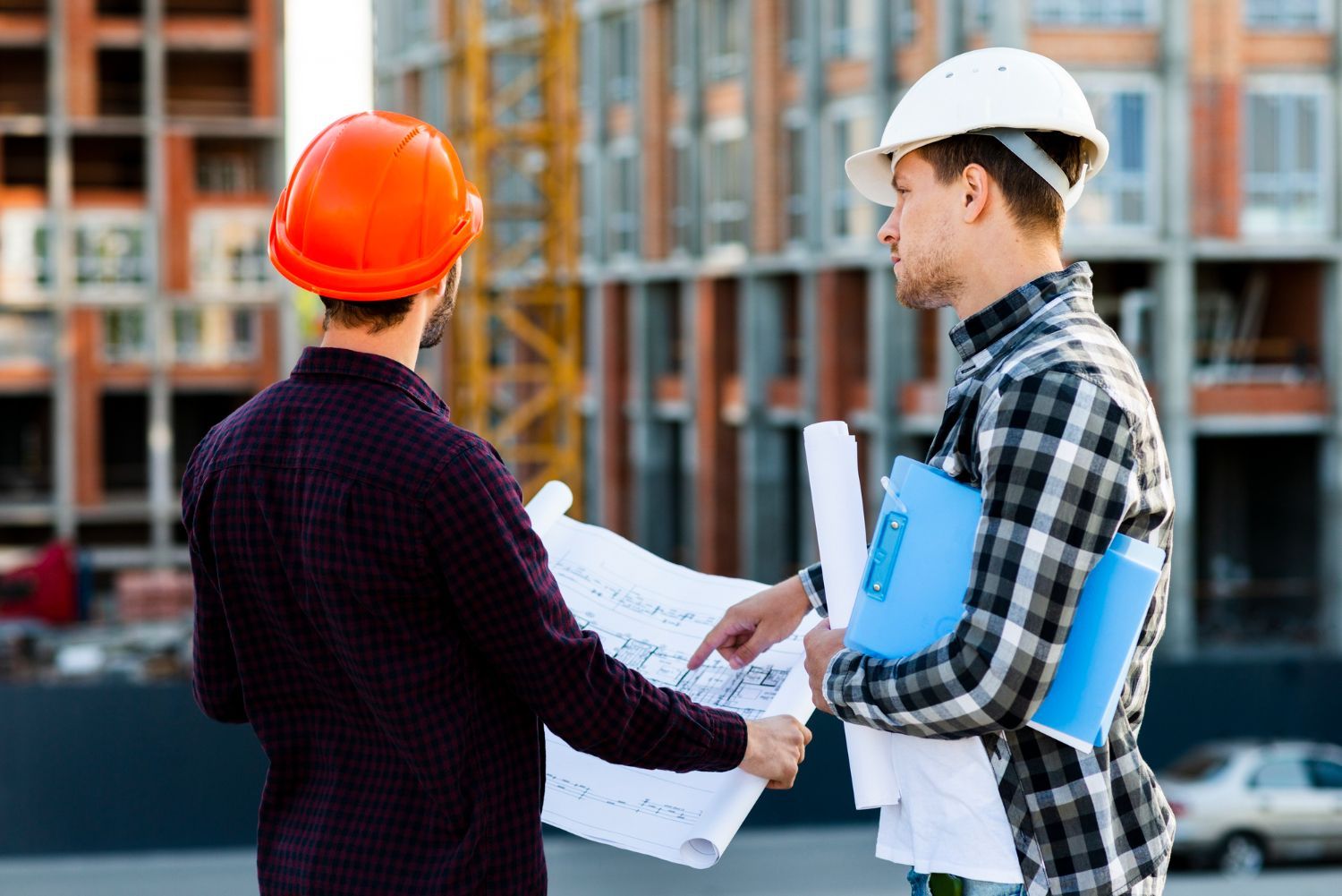 Two construction workers in hard hats reviewing blueprints at a building site