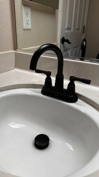 Black faucet with two handles over a white bathroom sink.