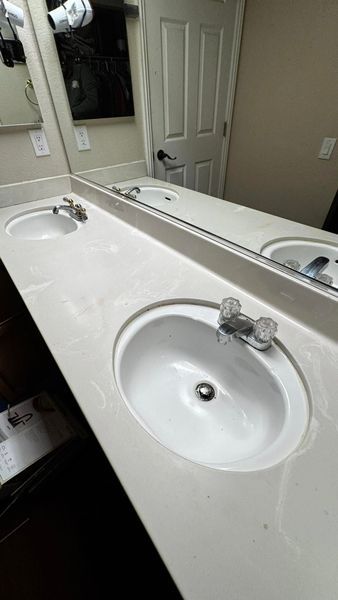 Bathroom with two white sinks on a light-colored countertop, large mirror, and closed white door.