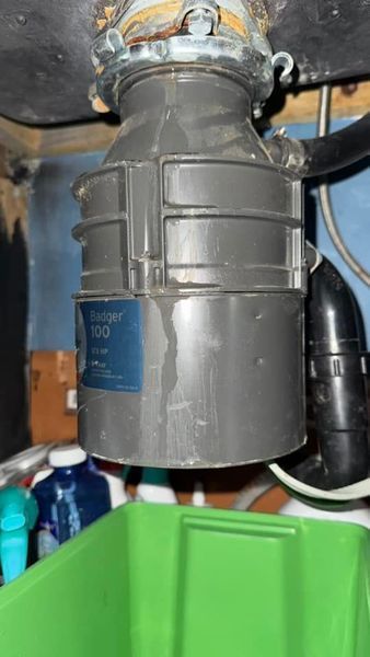 Gray garbage disposal with water stains under a kitchen sink.