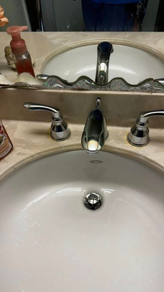 Bathroom sink with chrome faucet and handles, beige countertop, and a reflection in the mirror.