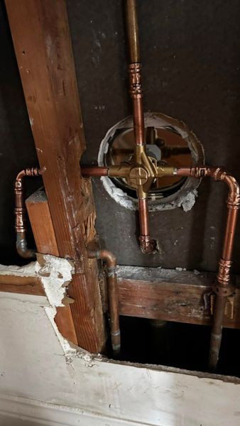 Copper plumbing pipes and valve assembly within a wall cavity, visible through an opening in the drywall.