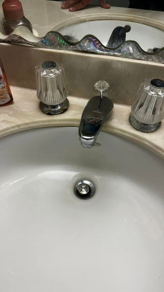 White bathroom sink with chrome faucet and two clear plastic handles.