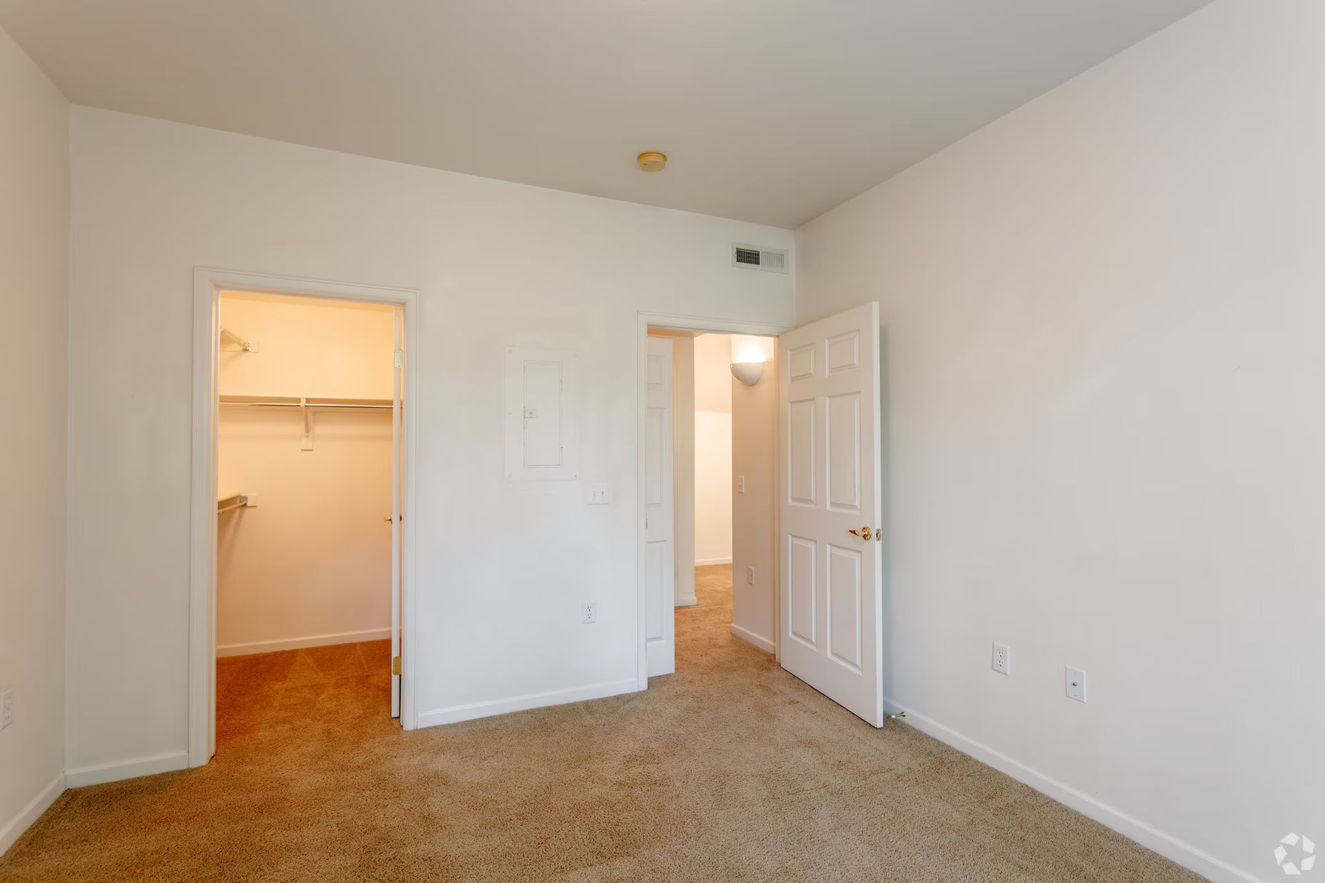 Empty beige bedroom with open closet and adjoining bathroom doorway