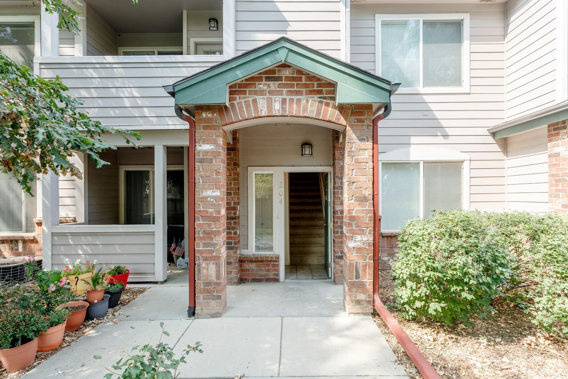 Front entrance of a brick-and-siding townhouse with a covered walkway and potted plants on both sides