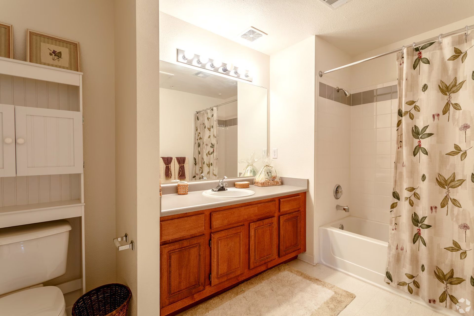 Bright bathroom with wood vanity, large mirror, and shower curtain with floral pattern.