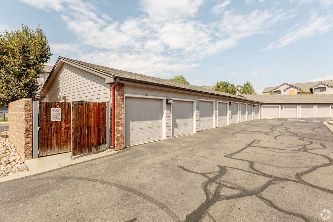 Row of white garage units with brown doors beside a cracked asphalt lot under a clear sky