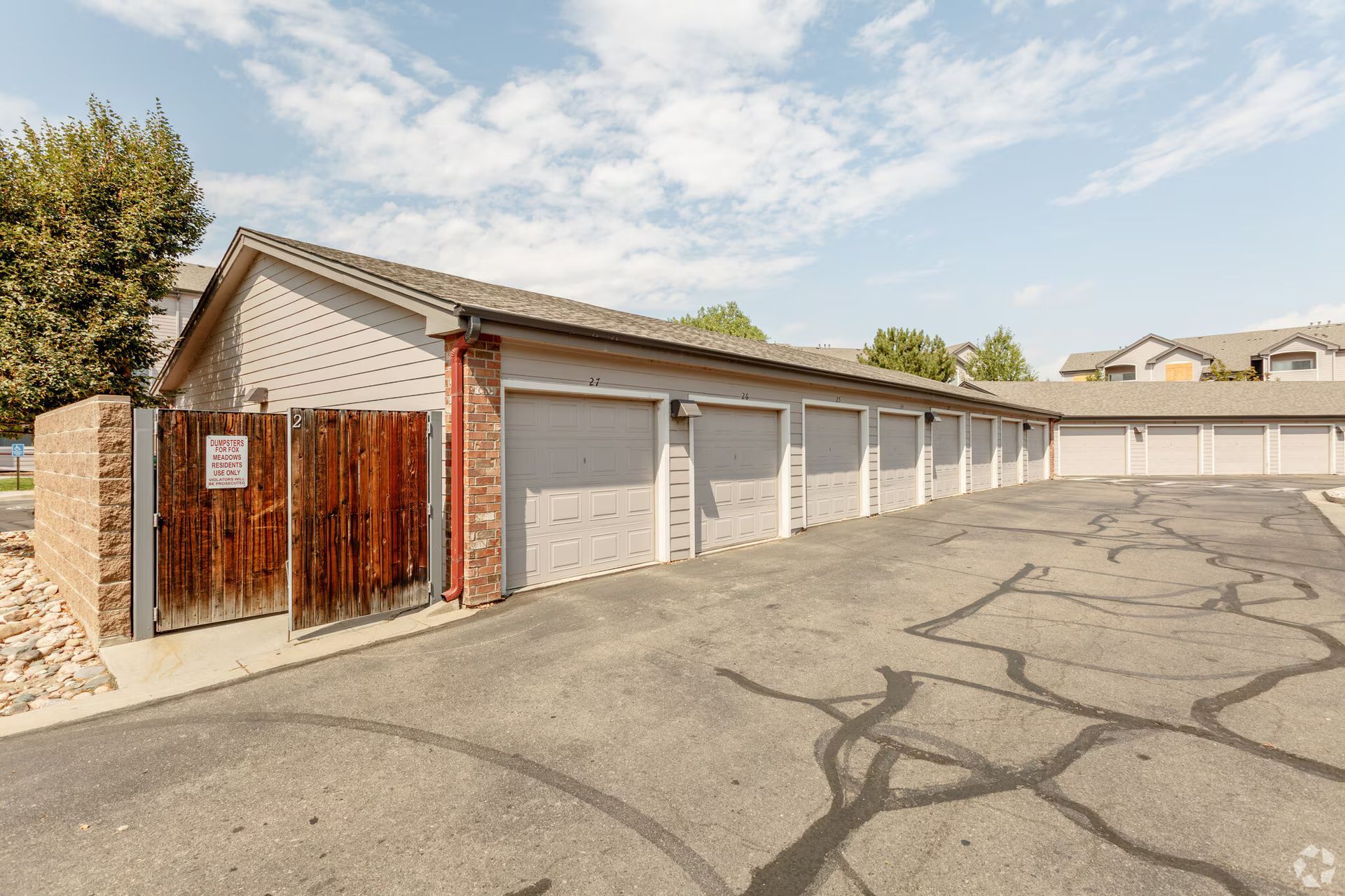Row of white garage units with wooden gate beside an empty asphalt lot under a clear sky