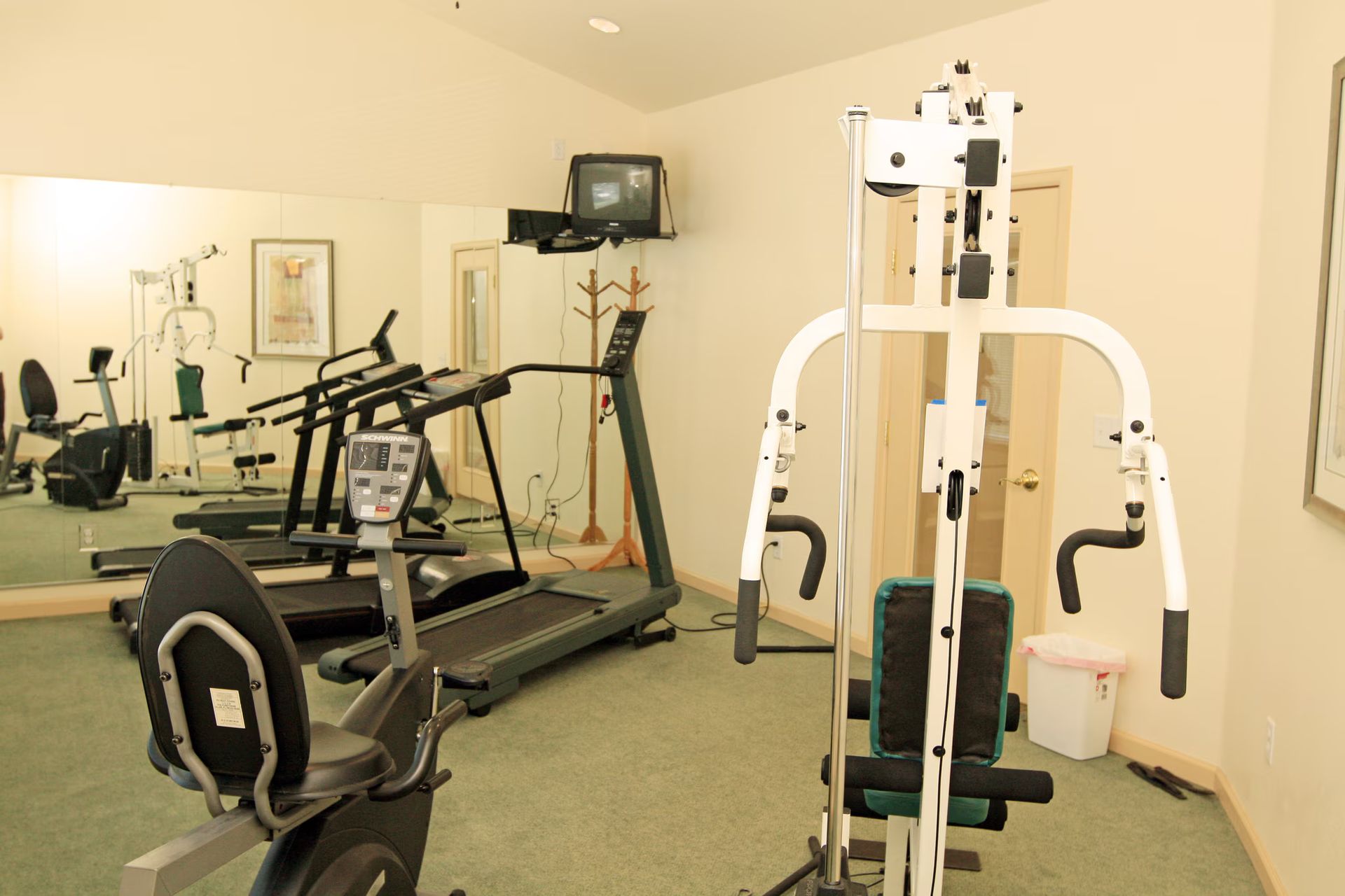 Gym room with exercise machines, mirrors, and beige walls.