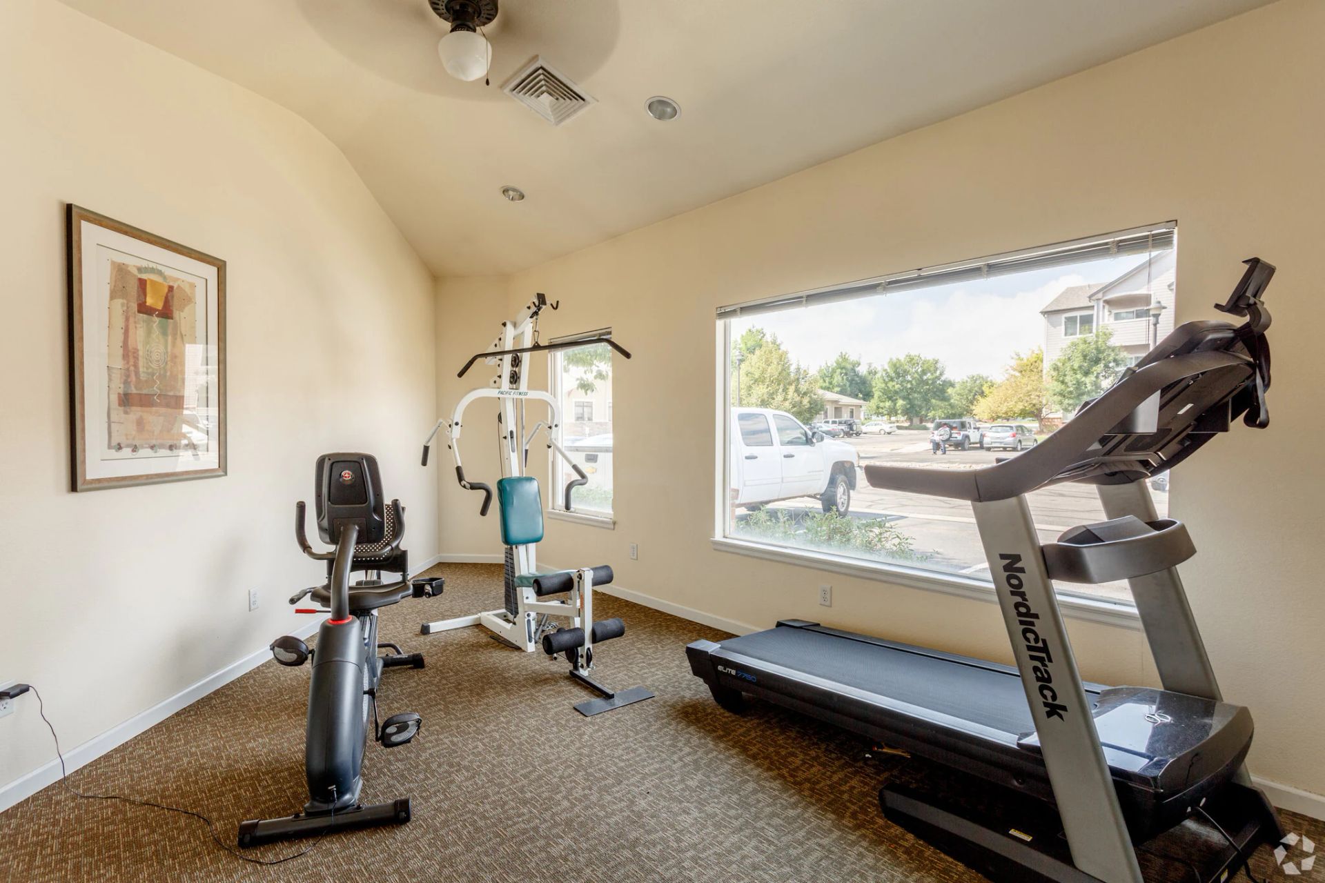 Home gym with treadmill, stationary bike, and weight machine beside a large window