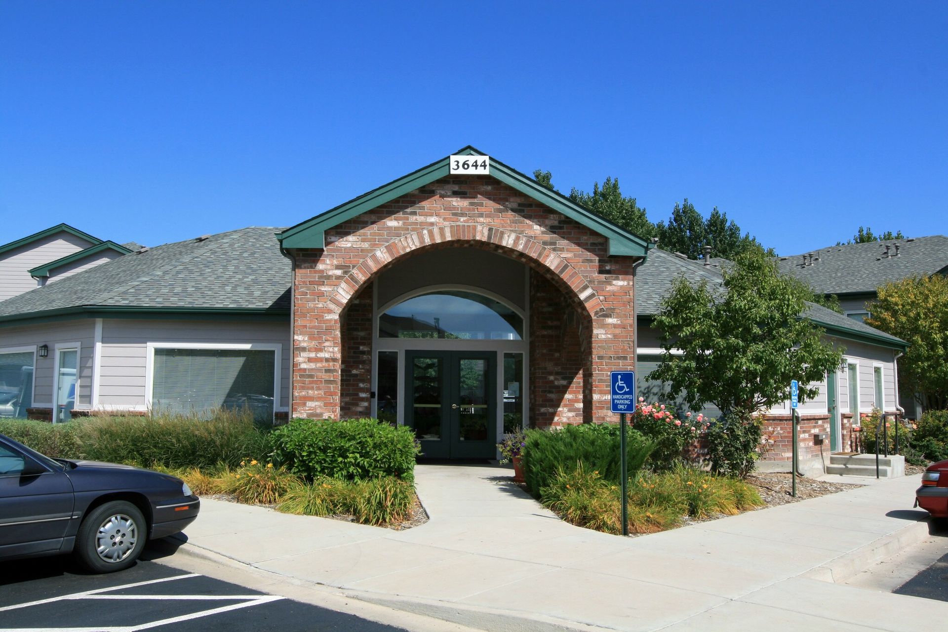 Brick building entrance with arched entry, glass doors, and parking lot in front