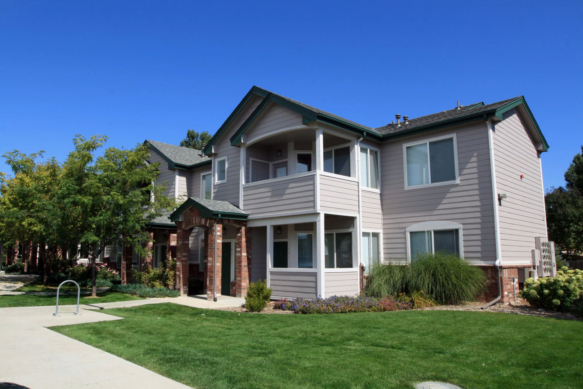 Apartment building with gray siding, balconies, and green lawn on a sunny day