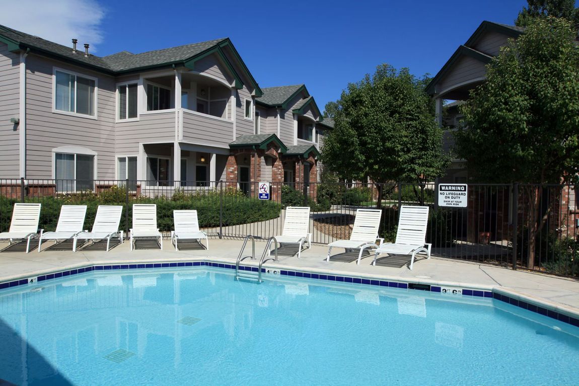 Apartment pool with white lounge chairs and tan buildings under a clear blue sky