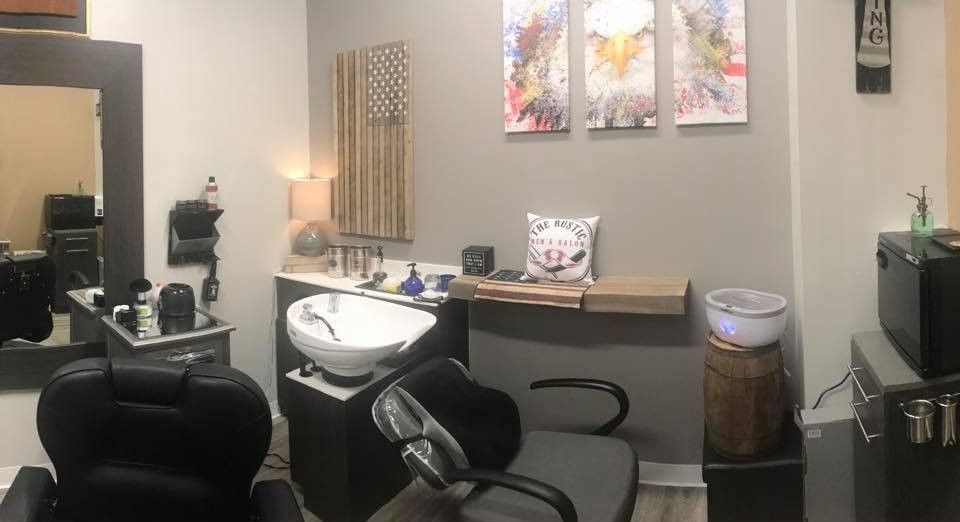 A salon area with a barber chair, a shampoo sink, a wooden American flag wall decor, and three abstract wall art pieces.