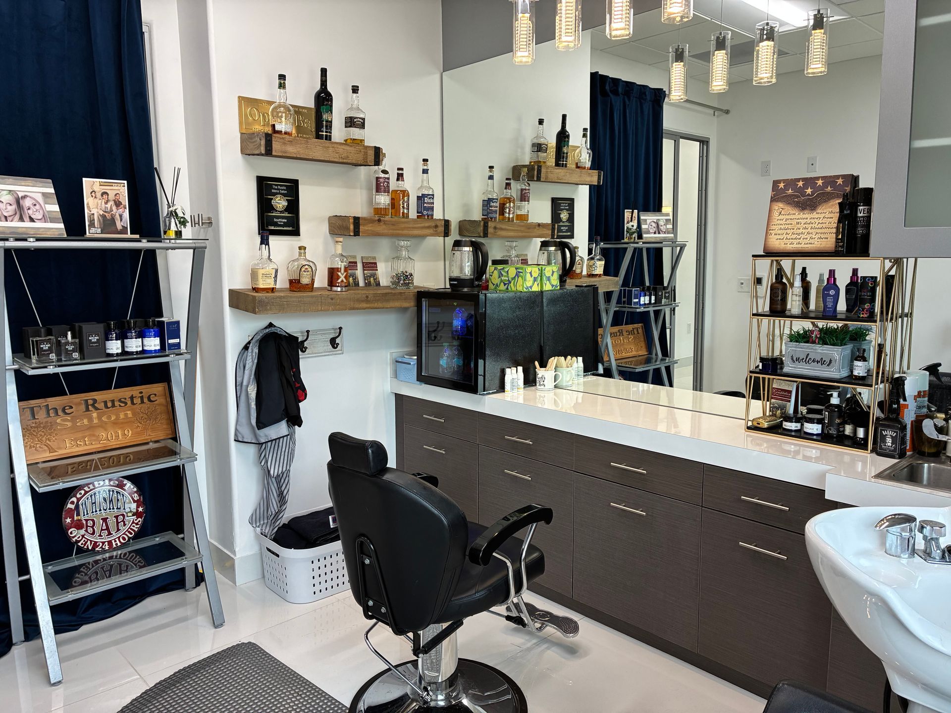 A modern salon station with a black barber chair, white counter, wall shelving with bottles, and a large mirror.