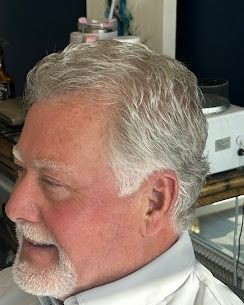 Side profile of a person with short, light hair and a trimmed beard, wearing a collared shirt in an indoor setting.