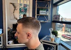 A side view of a person with a short, faded haircut in a hair salon with a mirror, shelves, and a large window.