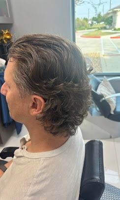 A person sits in a salon chair, showcasing a medium-length, wavy, layered haircut with grey and dark brown tones.