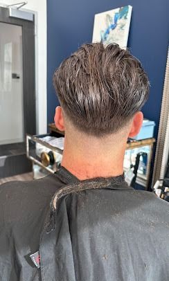 Back view of a short, textured haircut with a faded neckline, styled with product, in a salon setting.
