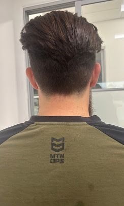 Back view of a person with a short-faded haircut, wearing an olive green and black athletic shirt.