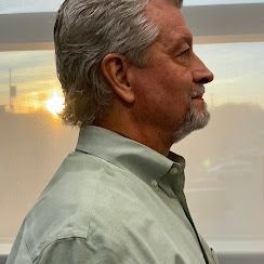 A person in a light green button-down shirt stands in profile, illuminated by sunlight through a nearby window.
